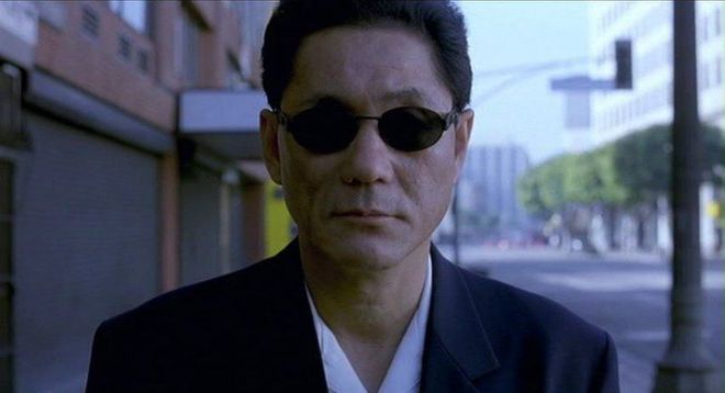 Photo of Takeshi Kitano, in black suit and dark sunglasses. Still from his film Brother.