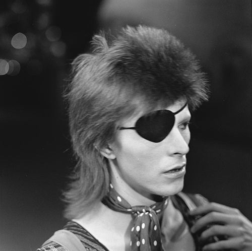 Black-and-white photo of young David Bowie wearing an eyepatch, via AVRO (Creative Commons).