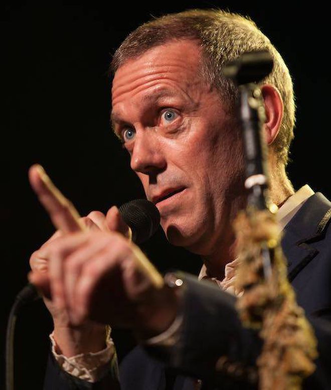 Close-up of man with short hair, holding a microphone, pointing his finger as if making a significant point